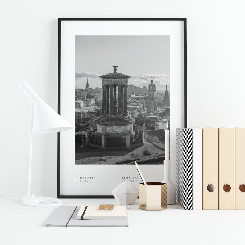 May include: Black and white photograph of the Edinburgh skyline featuring a monument and the city's iconic clock tower. The image is framed in a black frame and displayed on a white surface with office supplies.