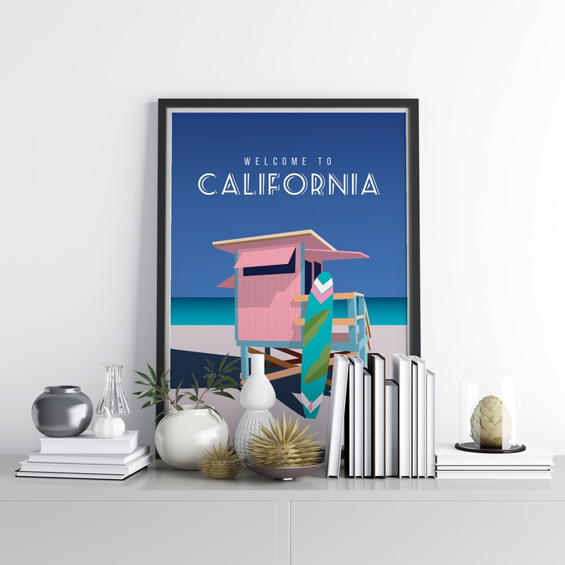 May include: A framed print with a blue background and a pink lifeguard stand with a surfboard leaning against it. The text "WELCOME TO CALIFORNIA" is at the top of the print.