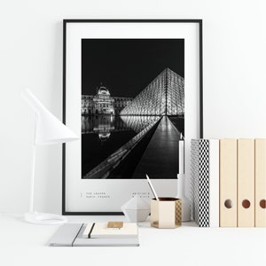 May include: Black and white photograph of the Louvre Museum in Paris, France at night. The iconic glass pyramid is illuminated, reflecting in the water. The text "THE LOUVRE PARIS, FRANCE" is at the bottom of the image.