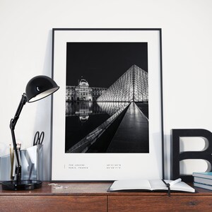 May include: Black and white photograph of the Louvre Museum in Paris, France at night. The iconic glass pyramid is reflected in the water in front of the building. The text "THE LOUVRE PARIS, FRANCE" is at the bottom of the image.