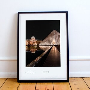 May include: A black and white photograph of the Louvre Museum in Paris, France at night. The iconic glass pyramid is illuminated and reflected in the water. The text "THE LOUVRE PARIS, FRANCE 48&deg;51'40"N 02&deg;20'11"E" is at the bottom of the image.