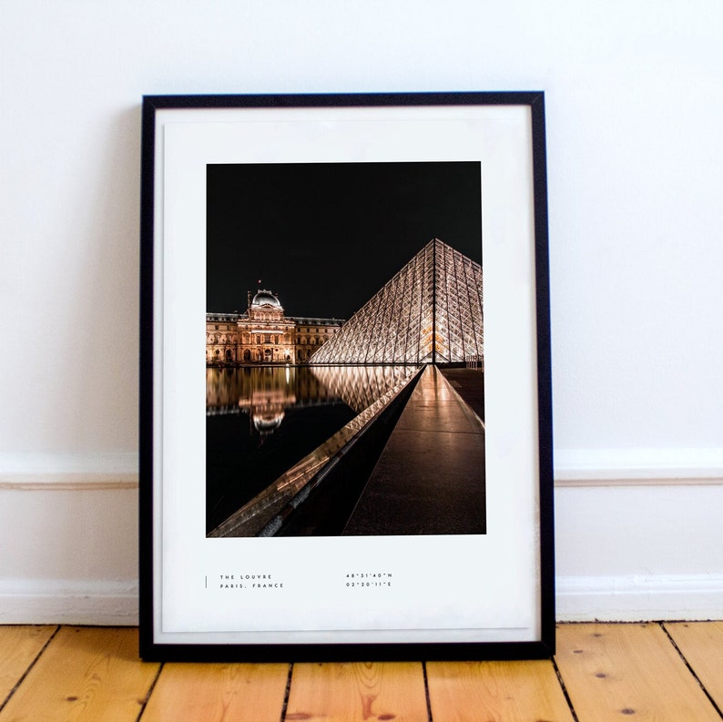 May include: A black and white photograph of the Louvre Museum in Paris, France at night. The iconic glass pyramid is illuminated and reflected in the water. The text "THE LOUVRE PARIS, FRANCE 48&deg;51'40"N 02&deg;20'11"E" is at the bottom of the image.