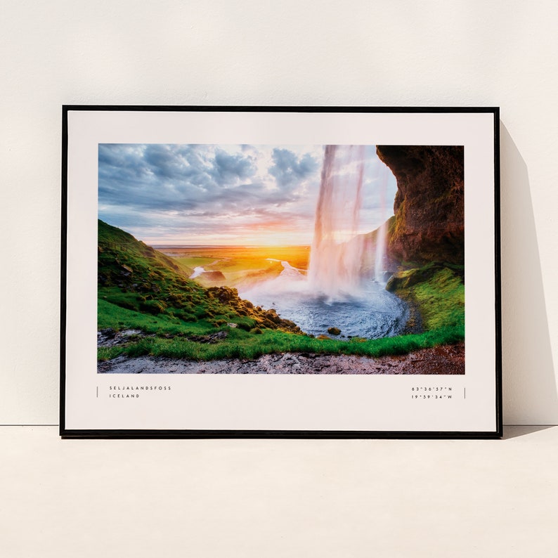 Op de afbeelding: Een ingelijste foto van de Seljalandsfoss-waterval in IJsland. De waterval stort neer over een klif met een zonsondergang op de achtergrond. De afbeelding bevat de co&ouml;rdinaten 63&deg;36'57"N 19&deg;58'34"W.