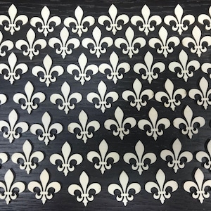 May include: A collection of white wooden fleur-de-lis shapes arranged in a repeating pattern on a black surface.