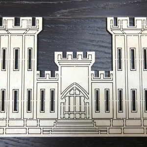 May include: A wooden cutout of a castle with two towers and a central building. The castle is detailed with windows and a door.