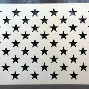 May include: A rectangular wooden panel with a pattern of black stars cut out against a light-colored background. The stars are evenly spaced, creating a visual representation of the American flag.