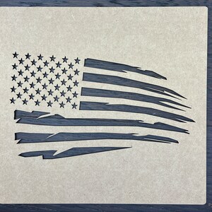 May include: A stencil of a distressed American flag. The flag is in a faded, worn look, with the stars and stripes appearing slightly torn and tattered.