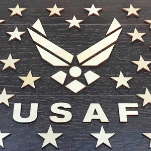 Könnte beinhalten: Holz-USAF-Emblem mit Sternen auf dunklem Holzgrund. Das Emblem zeigt das Air Force-Symbol und die Buchstaben "USAF" in hellem Holz. Die Sterne sind ebenfalls in hellem Holz gehalten.