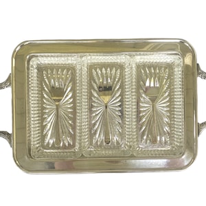 Puede incluir: Una bandeja rectangular plateada con tres compartimentos de vidrio transparente. Cada compartimento tiene un patrón decorativo en forma de abanico y un tenedor plateado. La bandeja tiene asas ornamentadas, ideal para servir aperitivos.
