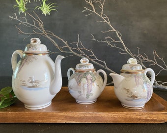May include: A set of three white porcelain teapots with gold and floral designs. The teapots are arranged on a wooden tray.
