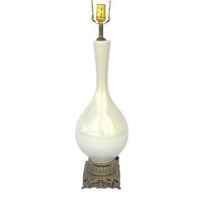 May include: A tall, off-white ceramic table lamp with a pear-shaped body and a slender neck. The lamp has a brass-colored base with ornate detailing and a standard lamp socket. The lamp is a decorative lighting fixture.