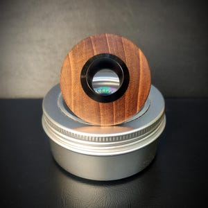 Puede incluir: Un anillo redondo de madera con un agujero central negro. El anillo está sentado encima de un recipiente plateado.