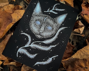 Può includere: Una stampa artistica nera raffigurante un volto di gatto stilizzato con accenti blu sulle orecchie e sugli occhi, e una luna crescente. Dettagli bianchi a forma di piuma e stelle circondano il volto del gatto. La stampa è su sfondo nero.