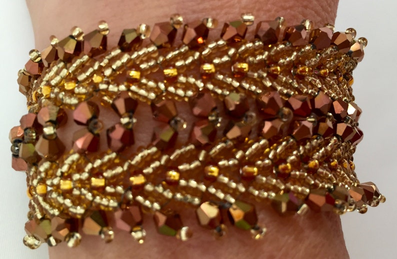 May include: A gold and copper beaded bracelet with a woven design. The bracelet is made with small, faceted beads in a variety of shades of gold and copper.
