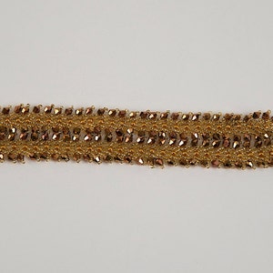 May include: A gold and brown beaded bracelet with a woven design. The bracelet has a clasp closure.