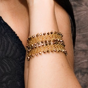May include: A gold beaded bracelet with a leaf-like design. The bracelet is made of small, round beads that are strung together in a pattern that resembles leaves. The beads are a mix of gold and brown colors.
