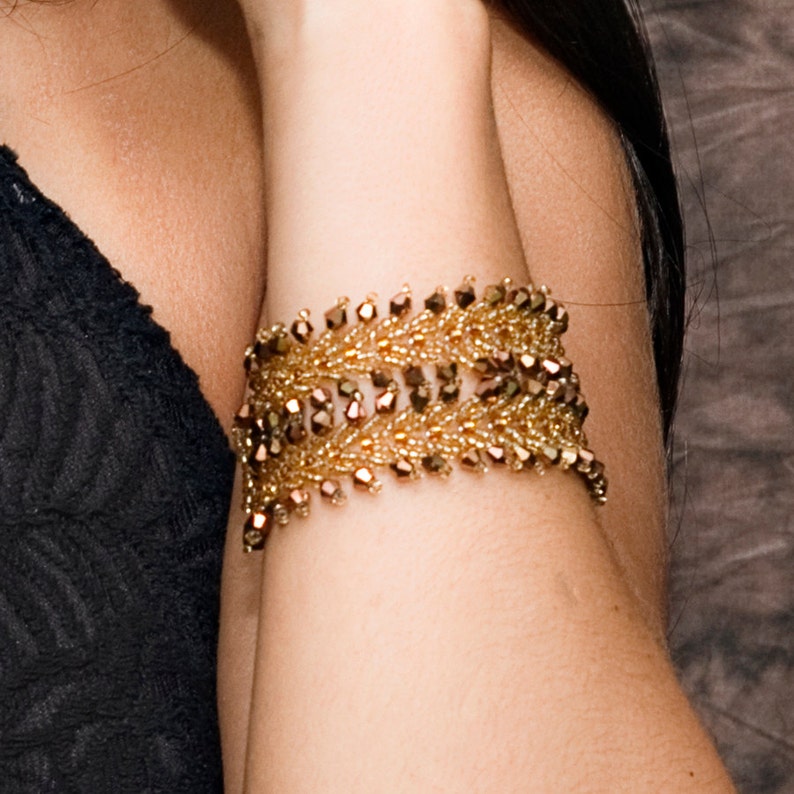 May include: A gold beaded bracelet with a leaf-like design. The bracelet is made of small, round beads that are strung together in a pattern that resembles leaves. The beads are a mix of gold and brown colors.