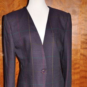 May include: A purple plaid blazer and skirt suit with a single button closure. The suit is on a mannequin and the background is a woodgrain pattern.