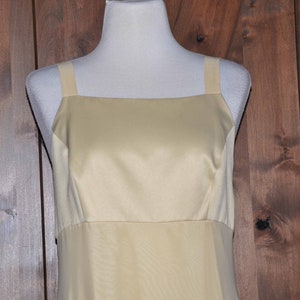 K&ouml;nnte beinhalten: Ein &auml;rmelloses, hellgelbes Satin-Kleid mit quadratischem Ausschnitt und einem schlichten, taillierten Oberteil.