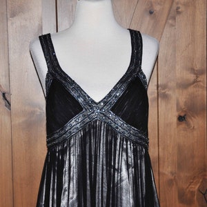 Puede incluir: Un vestido de noche negro con escote en V y tirantes finos. El corpi&ntilde;o est&aacute; adornado con lentejuelas y cuentas plateadas. La falda tiene un dise&ntilde;o fluido y plisado. El vestido se exhibe en un maniqu&iacute;.