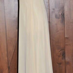 K&ouml;nnte beinhalten: Ein langes, elfenbeinfarbenes, &auml;rmelloses Kleid mit einem schlichten, eleganten Design. Das Kleid ist aus einem leichten, flie&szlig;enden Stoff gefertigt und hat einen taillierten Oberteil und einen flie&szlig;enden Rock.