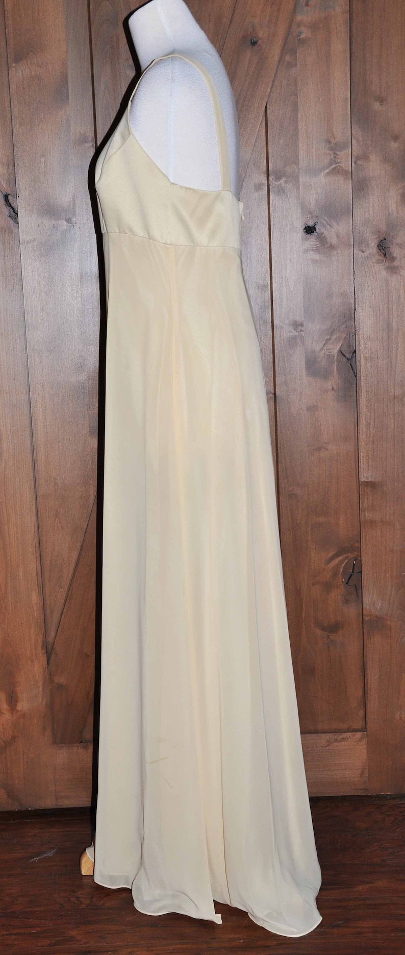 K&ouml;nnte beinhalten: Ein langes, elfenbeinfarbenes, &auml;rmelloses Kleid mit einem schlichten, eleganten Design. Das Kleid ist aus einem leichten, flie&szlig;enden Stoff gefertigt und hat einen taillierten Oberteil und einen flie&szlig;enden Rock.