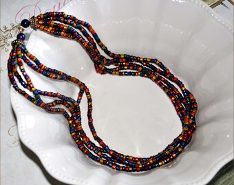 May include: Multi-strand necklace made of small, colorful beads. The beads are in shades of blue, green, orange, and red. The necklace is on a white plate.