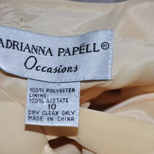 K&ouml;nnte beinhalten: Ein wei&szlig;es Etikett mit schwarzem Text, auf dem "ADRIANNA PAPELL Occasions" und "100% POLYESTER FUTTER: 100% ACETAT 10 NUR CHEMISCHE REINIGUNG HERGESTELLT IN CHINA" steht.