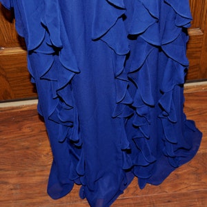 Puede incluir: Primer plano de un vestido azul real fluido con volantes en capas. Los volantes caen en cascada sobre la prenda, creando una apariencia texturizada y elegante. El vestido parece estar hecho de una tela ligera, adecuada para ocasiones formales.