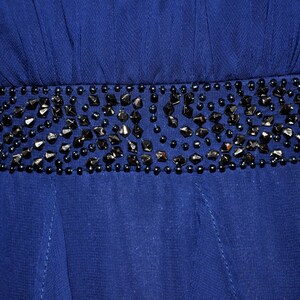 Puede incluir: Primer plano de un vestido azul oscuro con un cintur&oacute;n de cuentas. El cintur&oacute;n est&aacute; adornado con cuentas negras de forma irregular y cuentas redondas m&aacute;s peque&ntilde;as. La tela del vestido parece ser un material de gasa fluida.