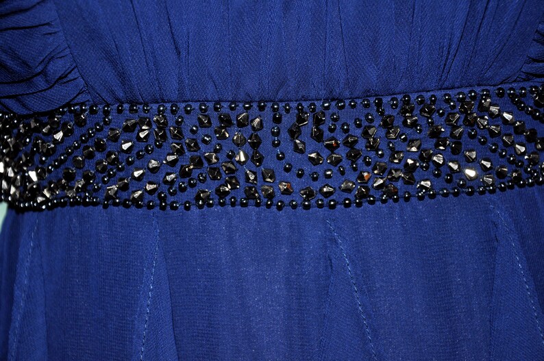 Puede incluir: Primer plano de un vestido azul oscuro con un cintur&oacute;n de cuentas. El cintur&oacute;n est&aacute; adornado con cuentas negras de forma irregular y cuentas redondas m&aacute;s peque&ntilde;as. La tela del vestido parece ser un material de gasa fluida.