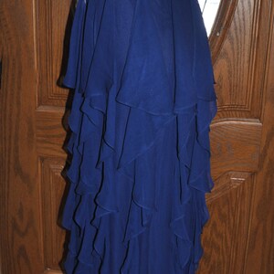 Puede incluir: Un vestido de noche azul marino sin tirantes con un cintur&oacute;n de cuentas. El vestido presenta una falda con volantes en capas. El corpi&ntilde;o est&aacute; fruncido y el vestido se exhibe en un maniqu&iacute;. El vestido mide aproximadamente 152 cm de largo.
