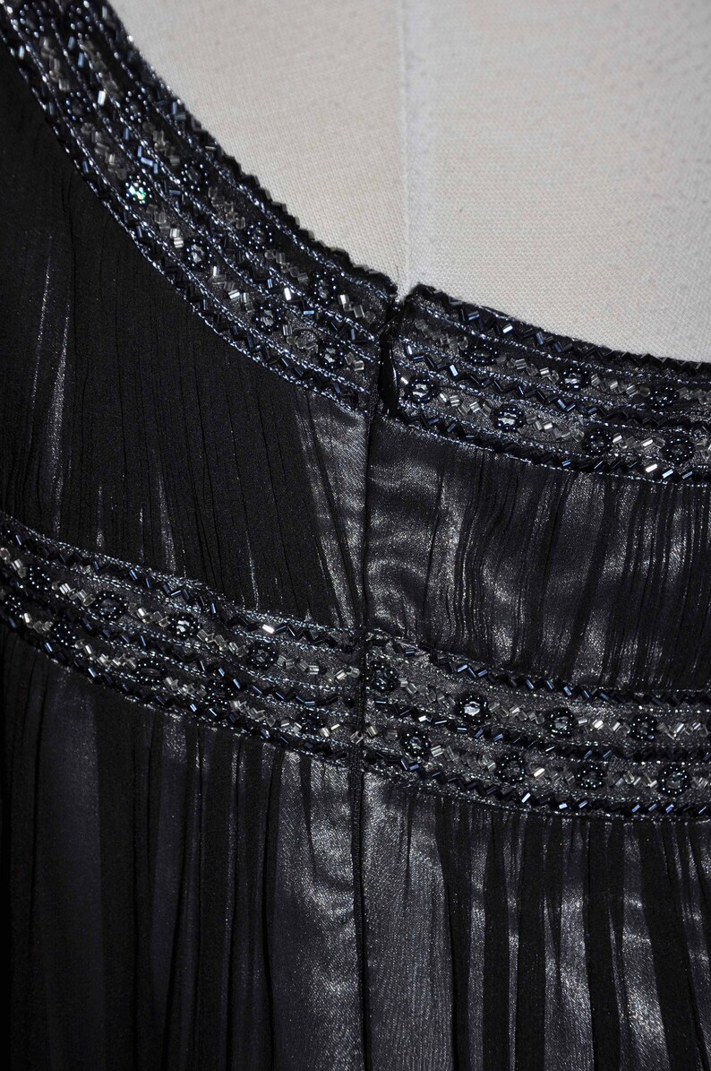 Puede incluir: Primer plano de un vestido negro con detalles de cuentas en el cuello y la cintura. El vestido tiene una tela transparente y fluida con l&iacute;neas verticales, y las cuentas son en tonos plateados y azul oscuro.