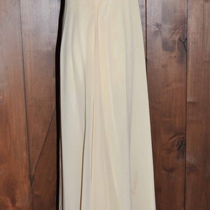 K&ouml;nnte beinhalten: Ein langes, &auml;rmelloses, elfenbeinfarbenes Kleid mit einem schlichten, figurbetonten Oberteil und einem flie&szlig;enden Rock.