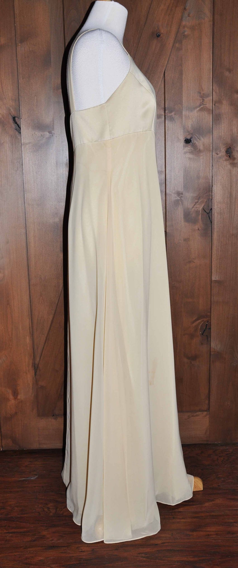 K&ouml;nnte beinhalten: Ein langes, &auml;rmelloses, elfenbeinfarbenes Kleid mit einem schlichten, figurbetonten Oberteil und einem flie&szlig;enden Rock.