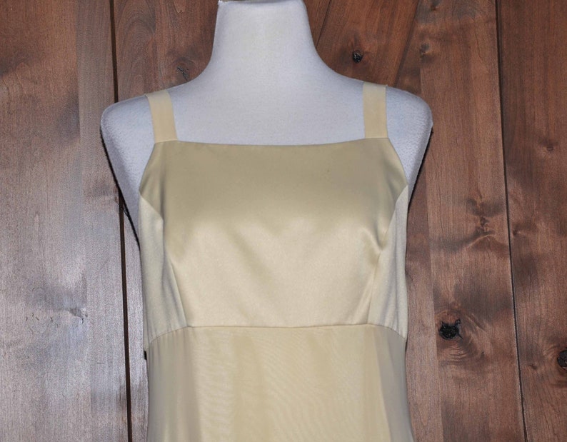 K&ouml;nnte beinhalten: Ein &auml;rmelloses, hellgelbes Satin-Kleid mit quadratischem Ausschnitt und einem schlichten, taillierten Oberteil.