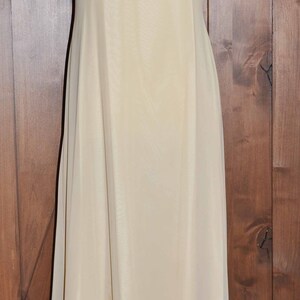K&ouml;nnte beinhalten: Ein &auml;rmelloses, bodenlanges, elfenbeinfarbenes Kleid mit einem einfachen, quadratischen Ausschnitt.