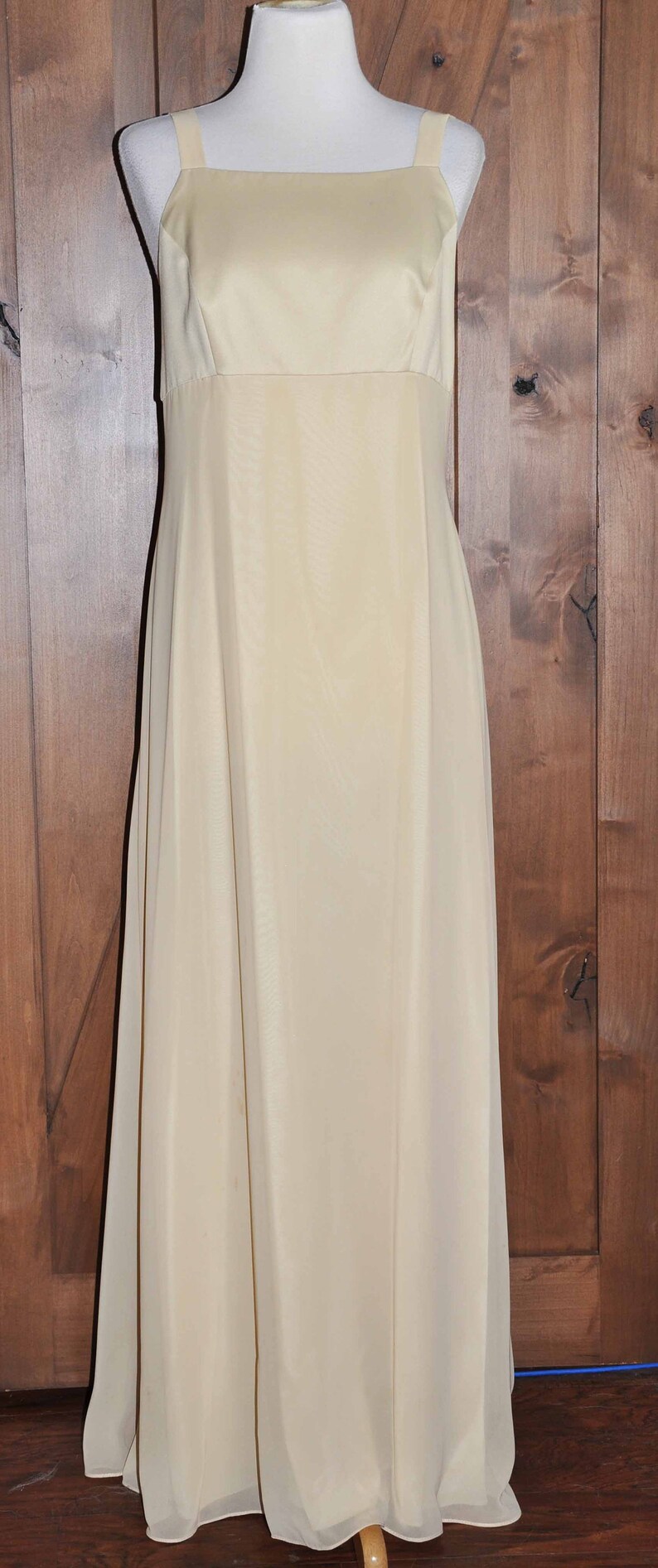 K&ouml;nnte beinhalten: Ein &auml;rmelloses, bodenlanges, elfenbeinfarbenes Kleid mit einem einfachen, quadratischen Ausschnitt.