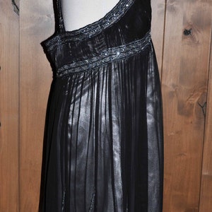Puede incluir: Vestido de noche negro con falda fluida y detalles de cuentas. El vestido presenta un cuello halter y delicadas cuentas a lo largo de las correas y la cintura. La falda es de tela transparente.