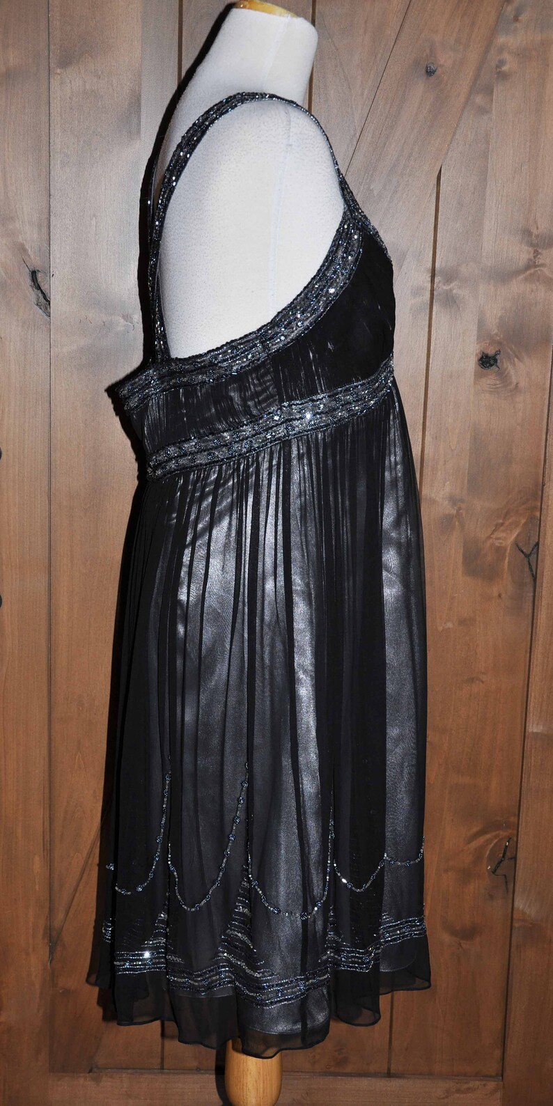 Puede incluir: Vestido de noche negro con falda fluida y detalles de cuentas. El vestido presenta un cuello halter y delicadas cuentas a lo largo de las correas y la cintura. La falda es de tela transparente.