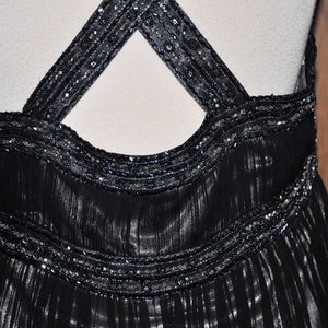 Puede incluir: Vestido de noche negro con cuello halter y tirantes cruzados en la espalda. Los tirantes y el corpi&ntilde;o est&aacute;n adornados con abalorios plateados. El vestido tiene una falda fluida y plisada, creando una silueta elegante.