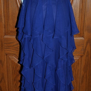 Puede incluir: Vestido de noche azul real sin tirantes, largo hasta el suelo, con falda con volantes en capas. El vestido se exhibe en un maniqu&iacute;, mostrando su elegante dise&ntilde;o y tejido fluido. La parte trasera del vestido tiene cierre de cremallera.