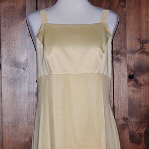 K&ouml;nnte beinhalten: Ein schlichtes, &auml;rmelloses, bodenlanges Kleid aus hellem gelbem Satin. Das Kleid hat einen quadratischen Ausschnitt und ein tailliertes Oberteil.