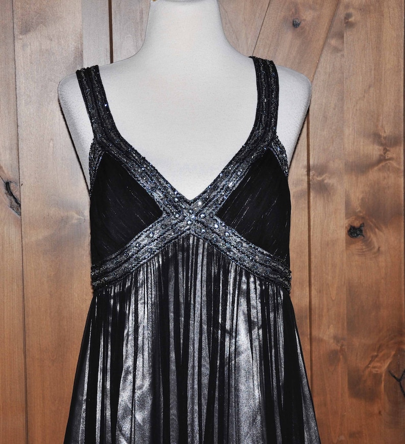 Puede incluir: Un vestido de noche negro con escote en V y tirantes finos. El corpi&ntilde;o est&aacute; adornado con lentejuelas y cuentas plateadas. La falda tiene un dise&ntilde;o fluido y plisado. El vestido se exhibe en un maniqu&iacute;.