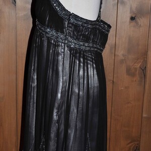 Puede incluir: Un vestido de noche negro con una falda fluida y en capas y adornos de cuentas. El vestido presenta un cuello halter y un corpi&ntilde;o ajustado con delicadas cuentas. La falda tiene un brillo sutil, y el dobladillo tambi&eacute;n est&aacute; adornado con detalles de cuentas.