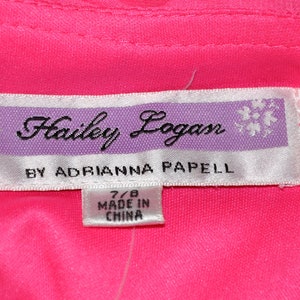以下が含まれることがあります： 紫色の縁取りのある白いタグに「Hailey Logan by Adrianna Papell」という文字と、「7/8 Made in China」と書かれた小さなタグが付いている。