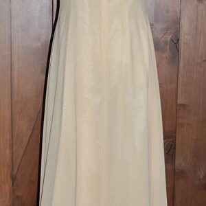 K&ouml;nnte beinhalten: Ein langes, &auml;rmelloses, elfenbeinfarbenes Maxikleid mit einem schlichten, geraden Ausschnitt. Das Kleid ist aus einem leichten, flie&szlig;enden Stoff gefertigt.