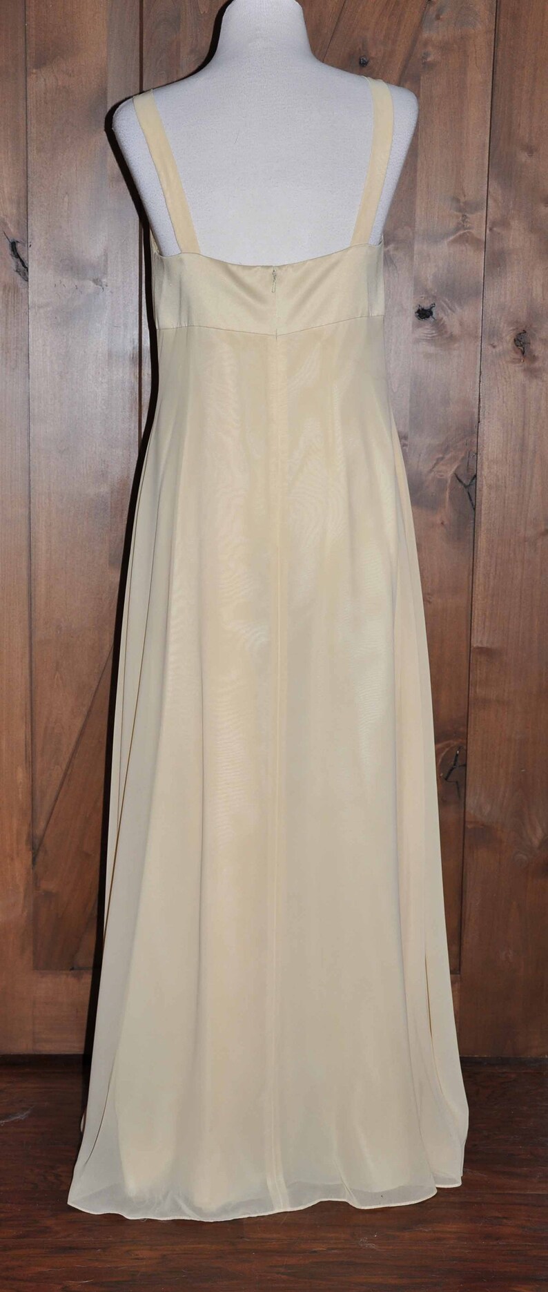 K&ouml;nnte beinhalten: Ein langes, &auml;rmelloses, elfenbeinfarbenes Maxikleid mit einem schlichten, geraden Ausschnitt. Das Kleid ist aus einem leichten, flie&szlig;enden Stoff gefertigt.
