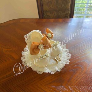 May include: Two white baby shoes with lace trim and orange satin bows. The shoes are on a white lace pillow.