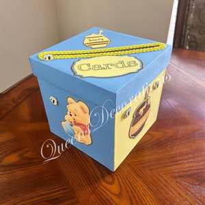 May include: A blue and yellow card box with a Winnie the Pooh character, a honey pot, and the word "Cards" on the top.